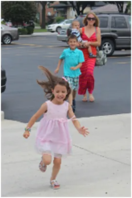 Girl in pink dress running; family walking outside near cars.