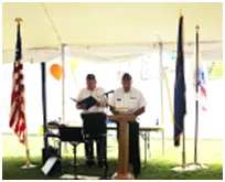 Two men in uniform speaking at a podium with flags.