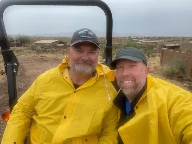 Two men wearing yellow raincoats are posing for a picture.