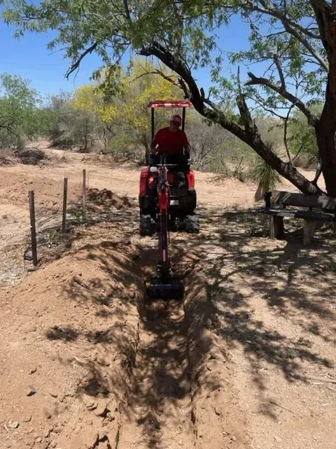 A man is driving a red tractor in a dirt field