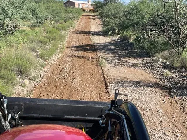 A person is driving a tractor down a dirt road.