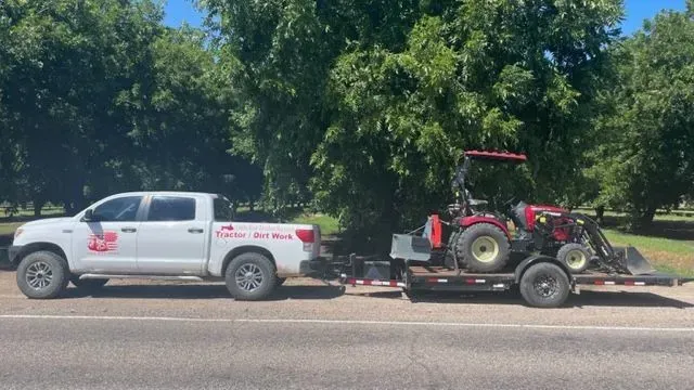 A white truck is towing a red tractor on a trailer.
