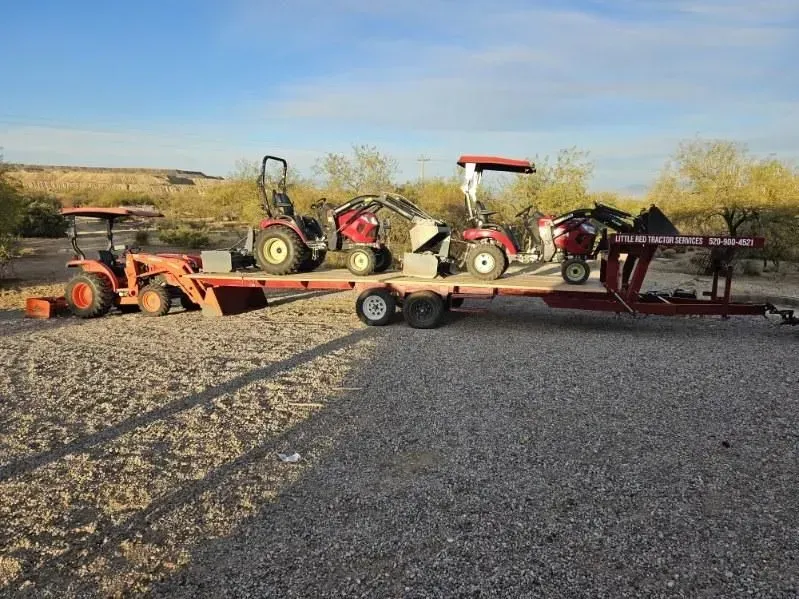 Three tractors are sitting on a trailer in a gravel lot.