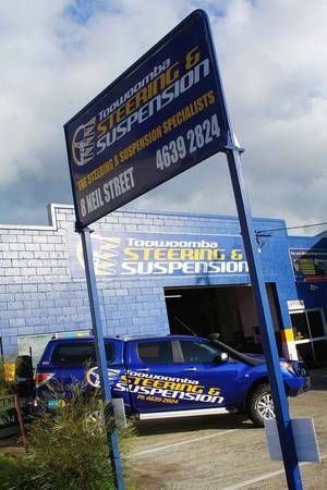 A blue sign and a matching blue pickup truck at a Toowoomba Steering & Suspension service center.