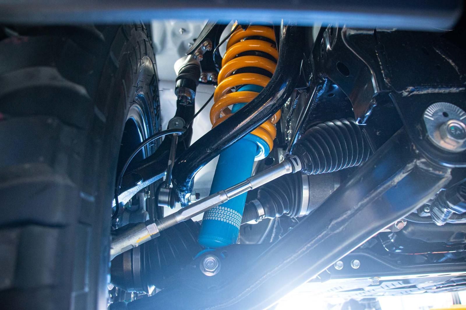 Close-up of a vehicle's underside, featuring a bright yellow coil spring and a blue shock absorber.