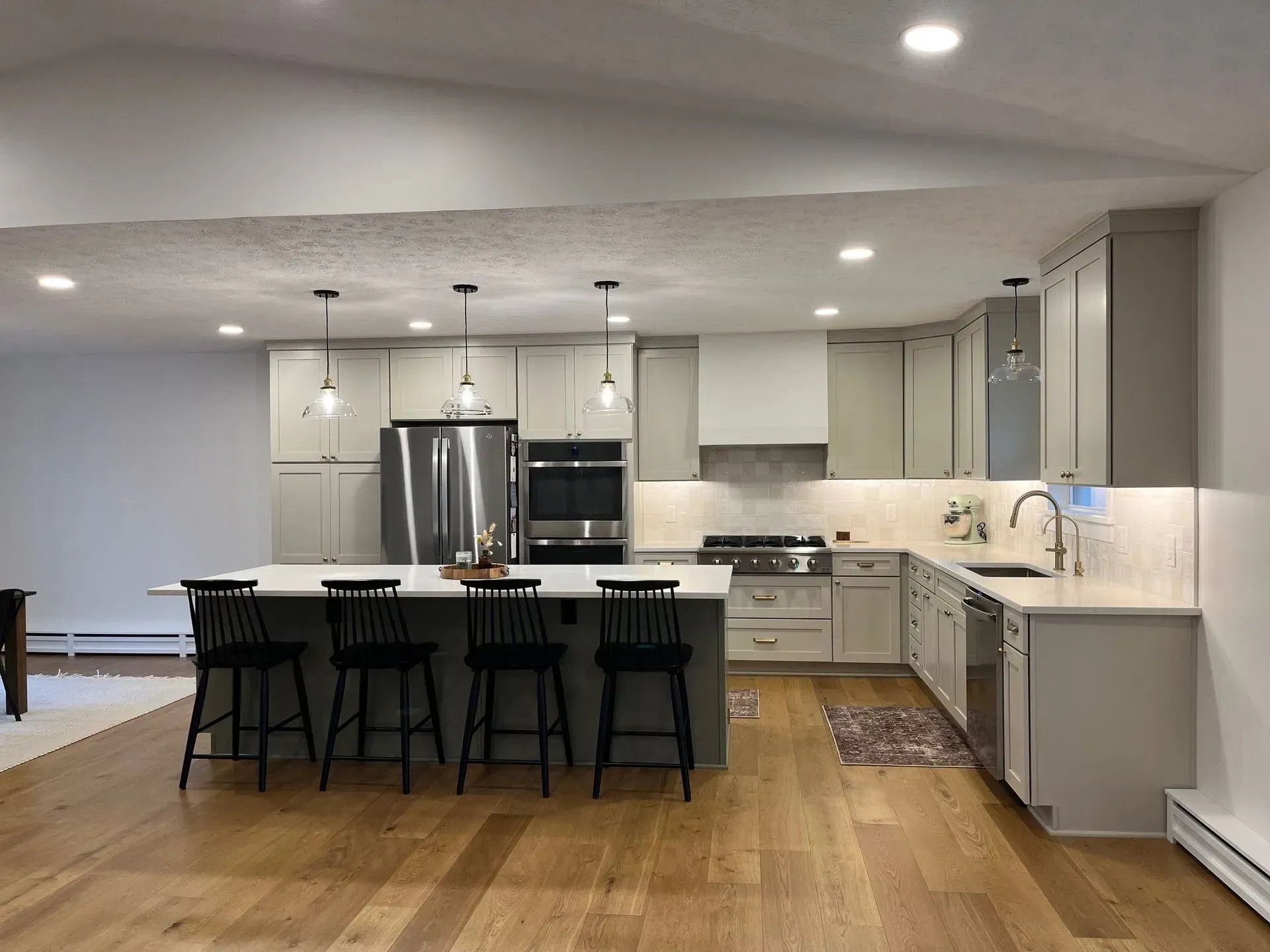 Modern kitchen with island and light gray cabinets, stainless steel appliances, and wood flooring.