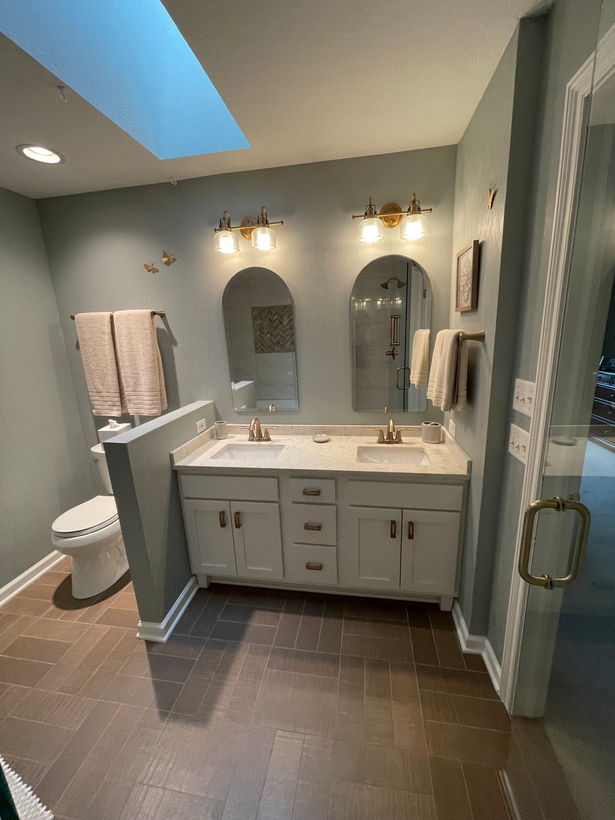 Dark marble shower with glass doors in a bathroom. White tub in the foreground, wood paneling on the right.