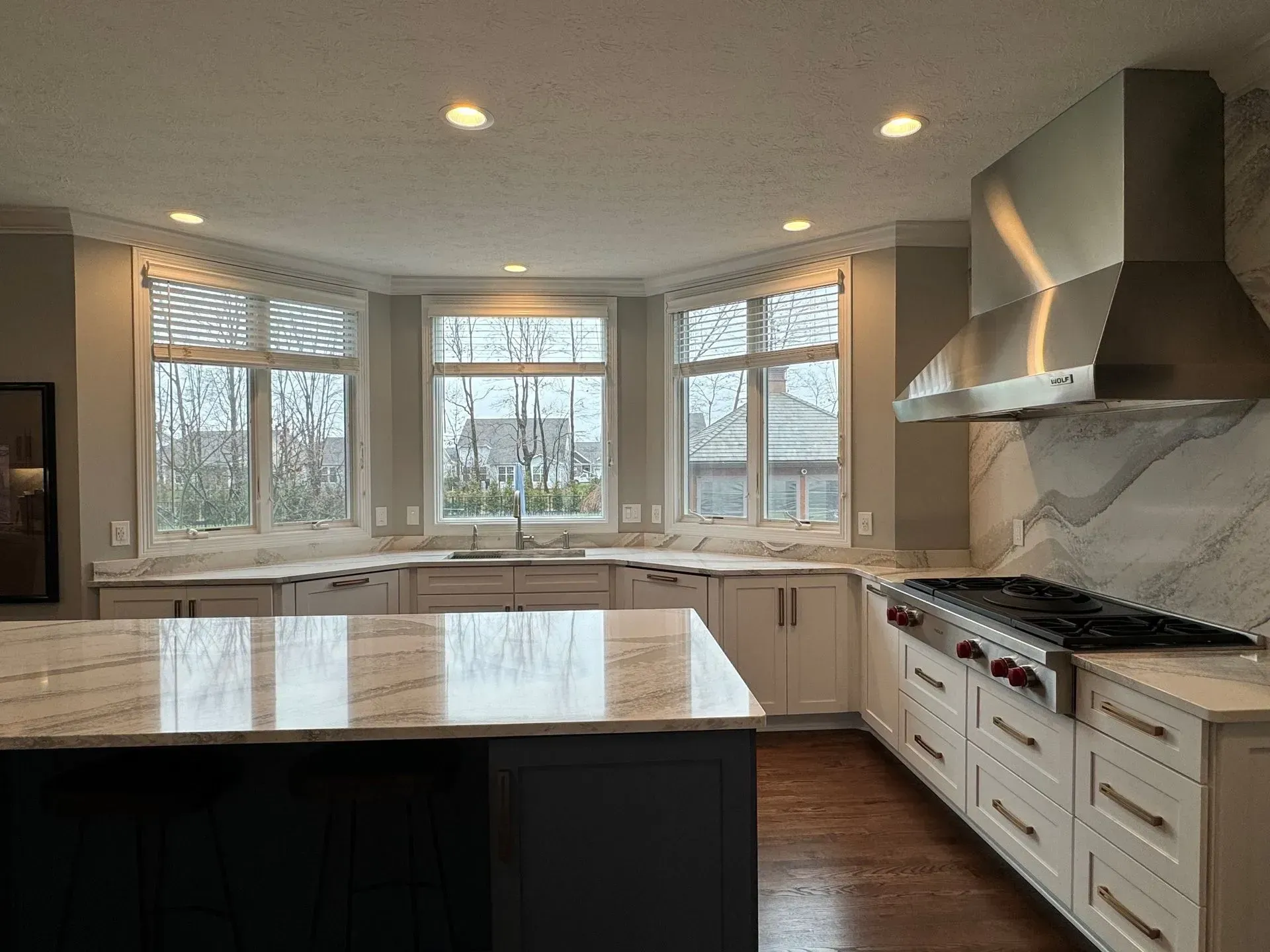 Modern kitchen with white cabinets, marble countertops, stainless steel range hood, and large windows.