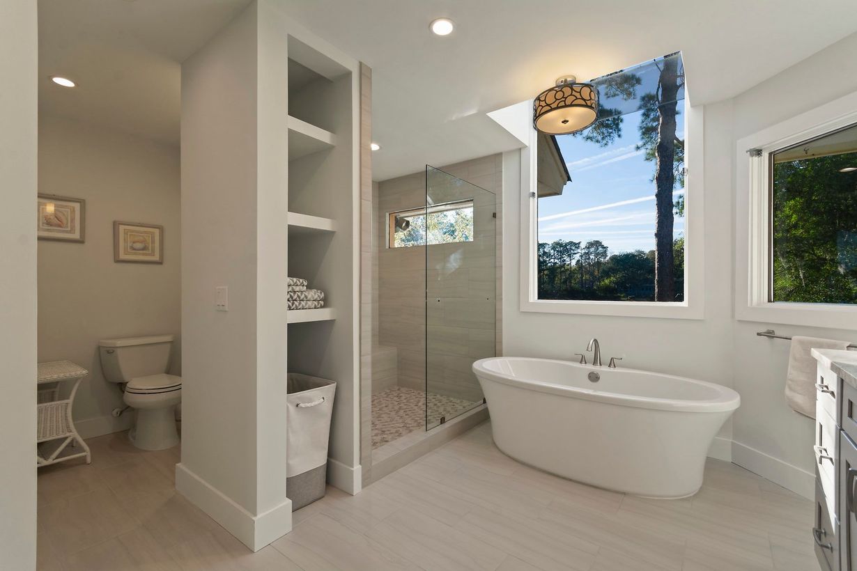 Dark marble shower with glass doors in a bathroom. White tub in the foreground, wood paneling on the right.