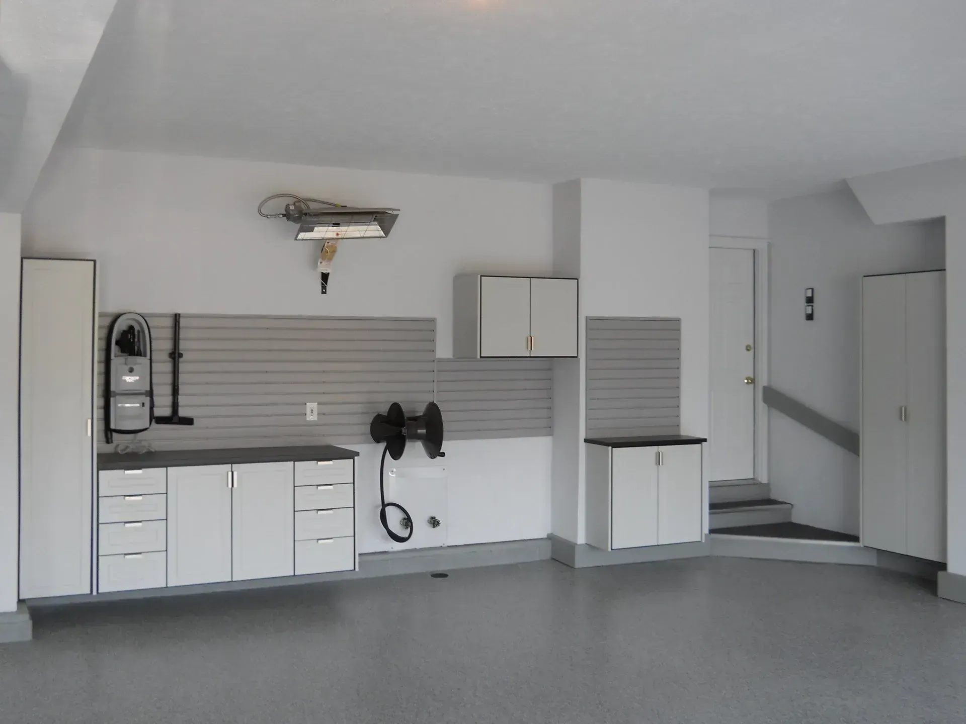 White garage with cabinets, work surface, and gray slat wall.