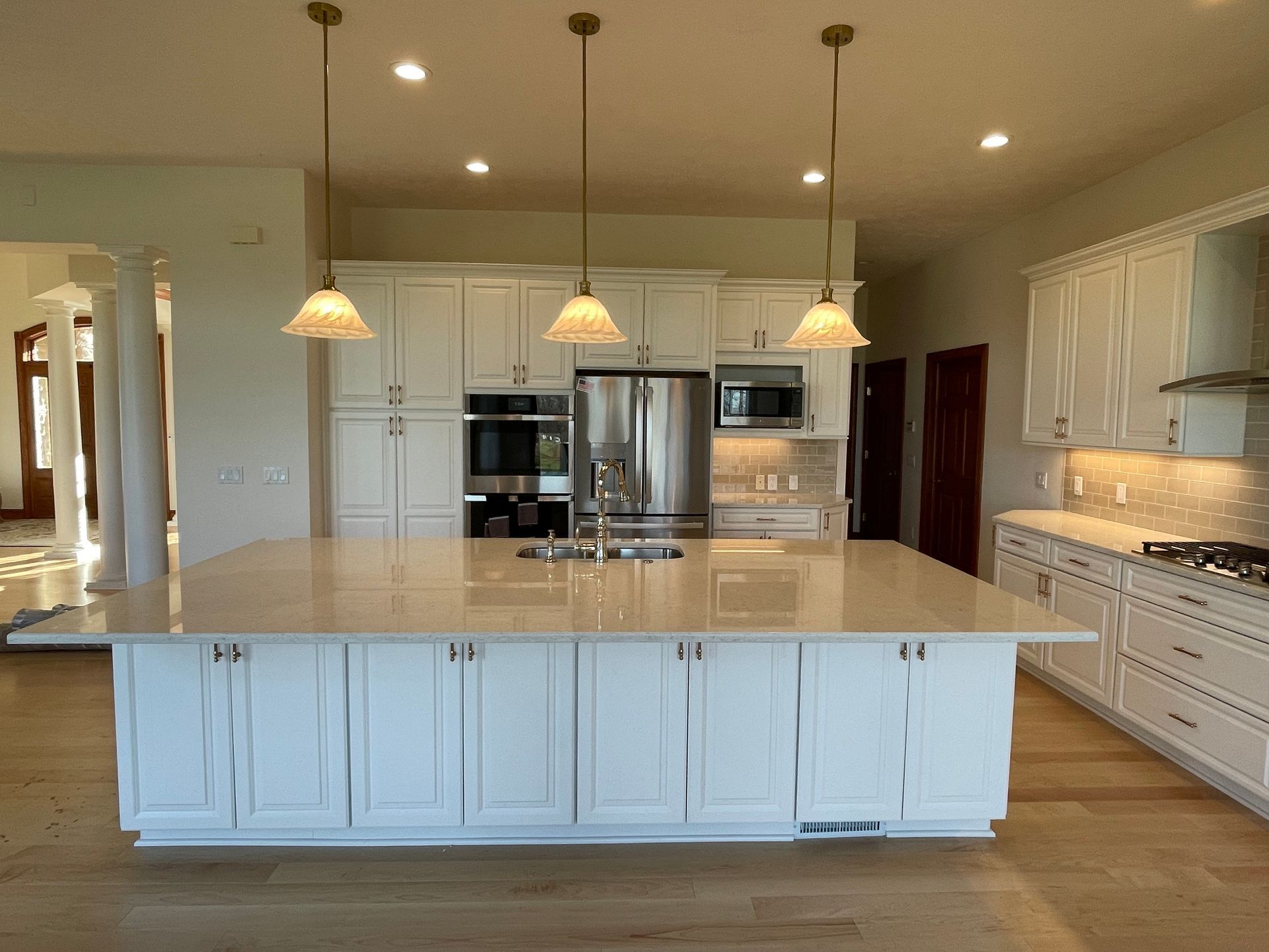 White kitchen with large island, pendant lights, stainless steel appliances, and wood floors.