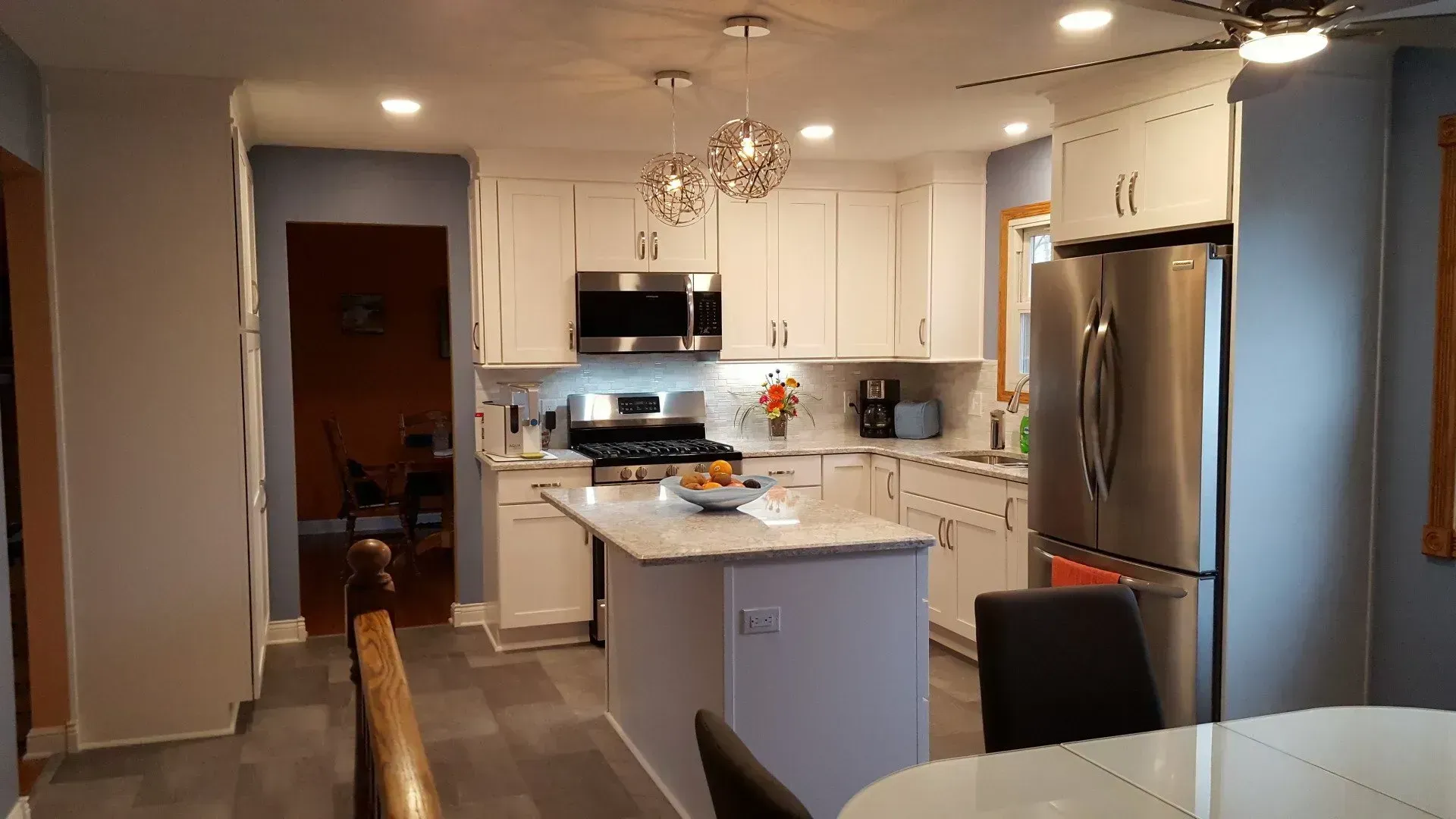Modern white kitchen with island, stainless steel appliances, and gray flooring.