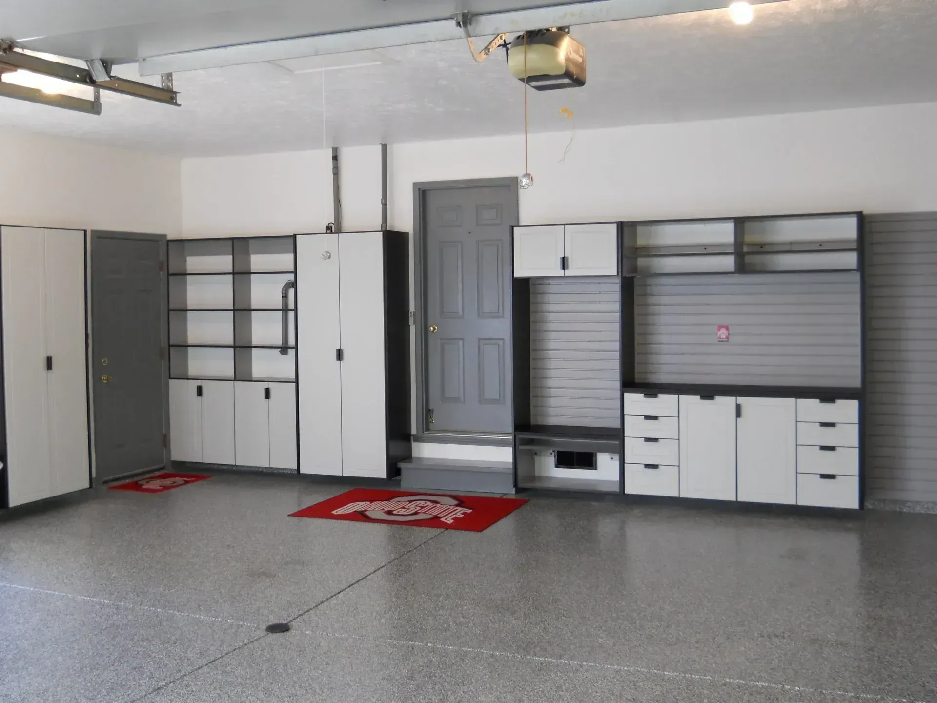 Garage with organized storage cabinets and shelves, gray and white, with a door and epoxy floor.