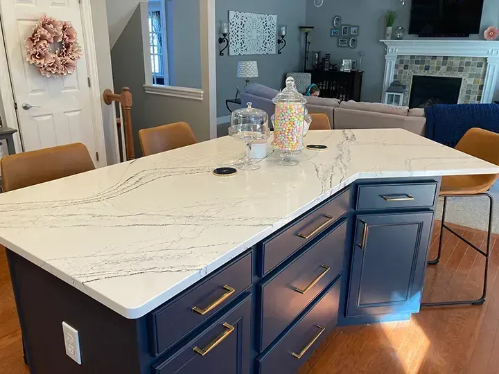 Kitchen island with white countertops, navy cabinets, gold handles, and bar stools.