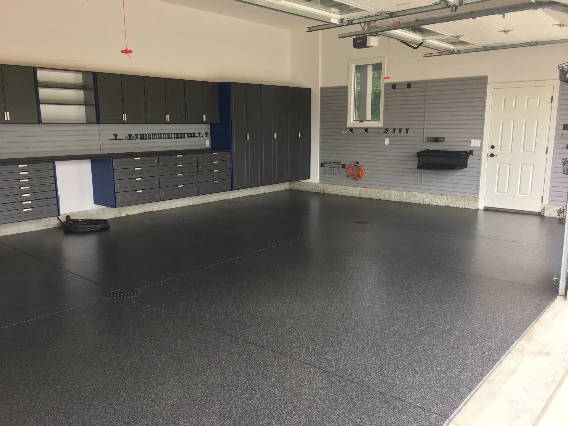A spacious garage with a dark gray epoxy floor, gray cabinets, and a white door.