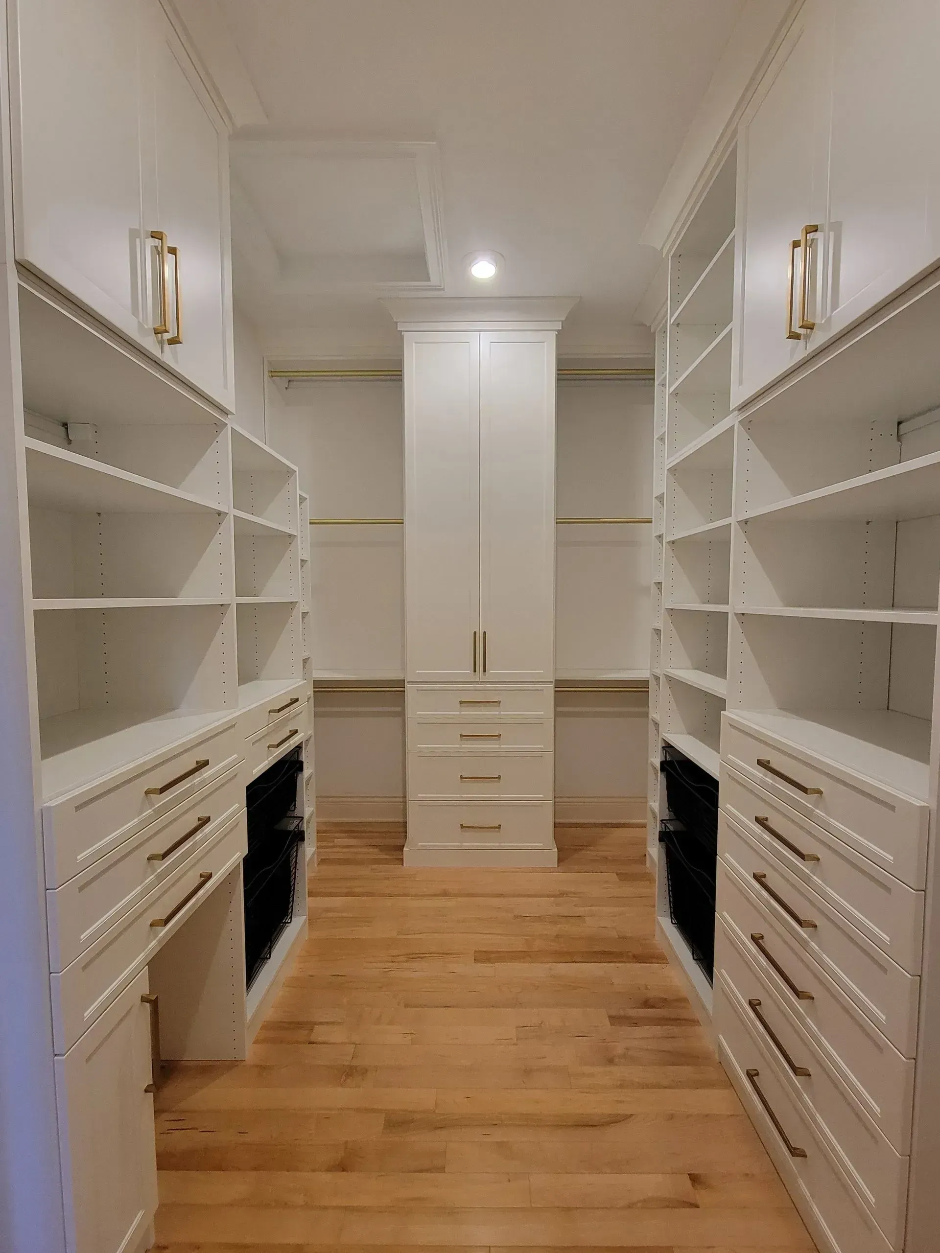 White walk-in closet with shelves, drawers, and a tall cabinet; hardwood floor.