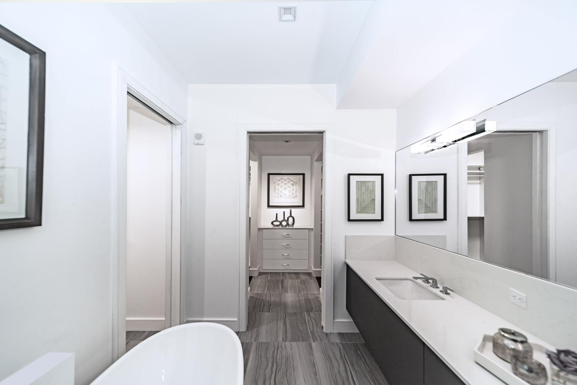 Modern bathroom with gray and white color scheme, wood-look floor, sink, bathtub, and artwork.
