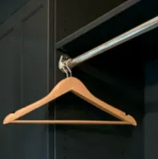 Wooden hanger hanging from a metal rod in a dark closet.