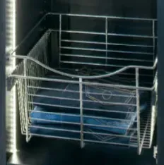 A wire basket inside a dark cabinet holds folded blue jeans.