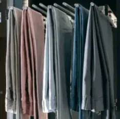 Pants hanging on a pull-out rack; various colors, close-up in a closet.