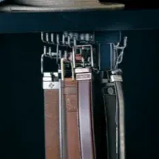 Belts hanging on a metal rack attached to a dark shelf.
