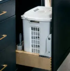 Laundry basket in a pull-out cabinet, inside a dark blue cabinet.