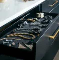Open drawer displaying jewelry on a dark gray felt-lined surface; gold drawer pulls.