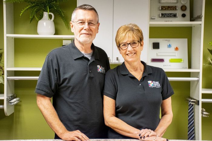 Two people, a man and woman, pose in front of shelves, both wearing matching black shirts.