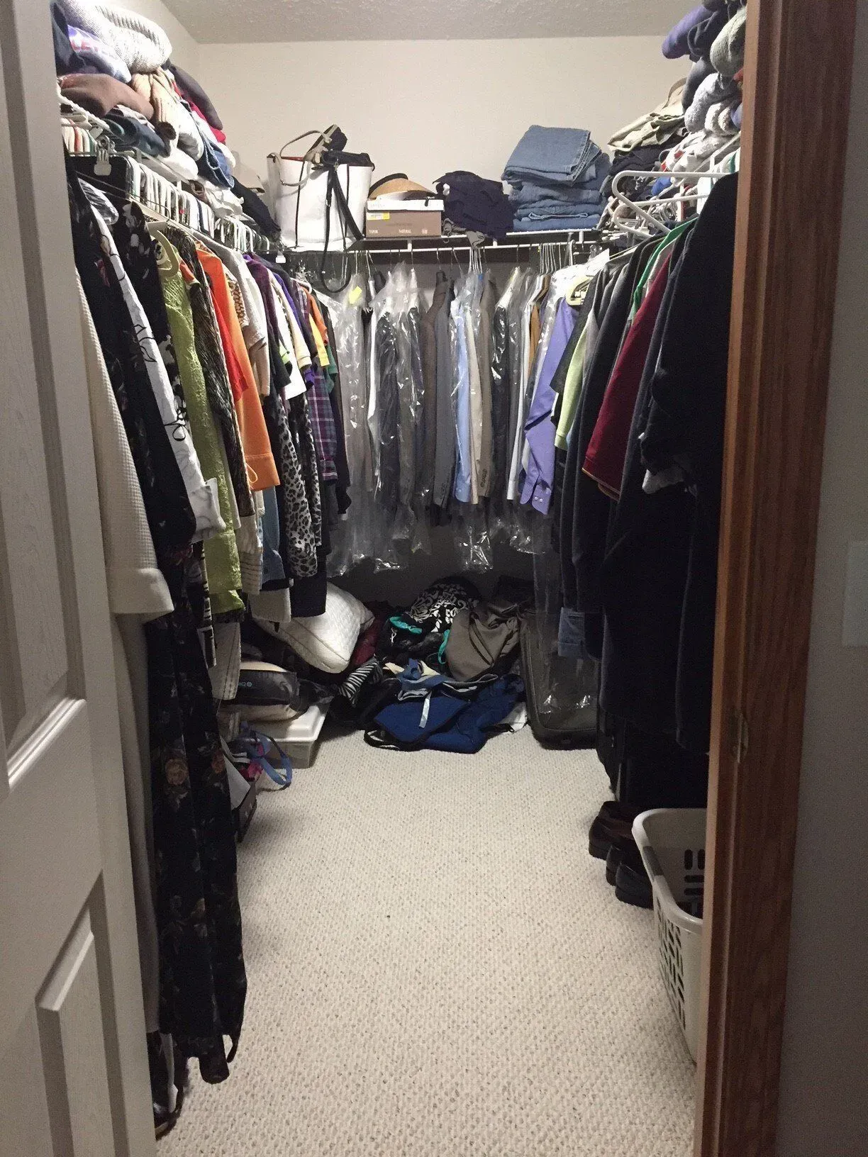 A cluttered walk-in closet with clothes hanging and items piled on shelves and the floor.