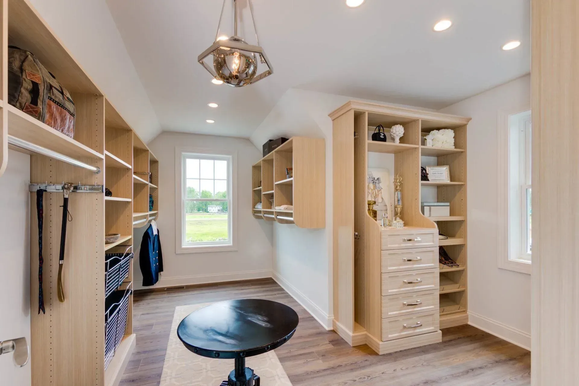 Walk-in closet with light wood shelving, a central table, and a decorative light fixture.