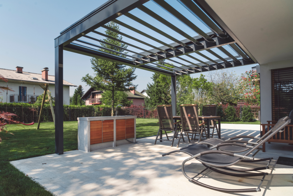A patio with chairs , tables and a pergola in the backyard.
