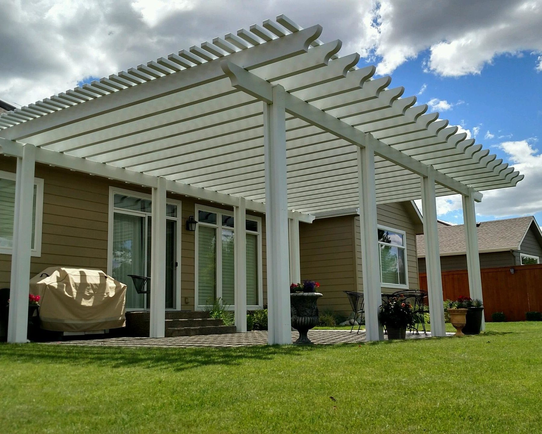 A white pergola is sitting in front of a house.