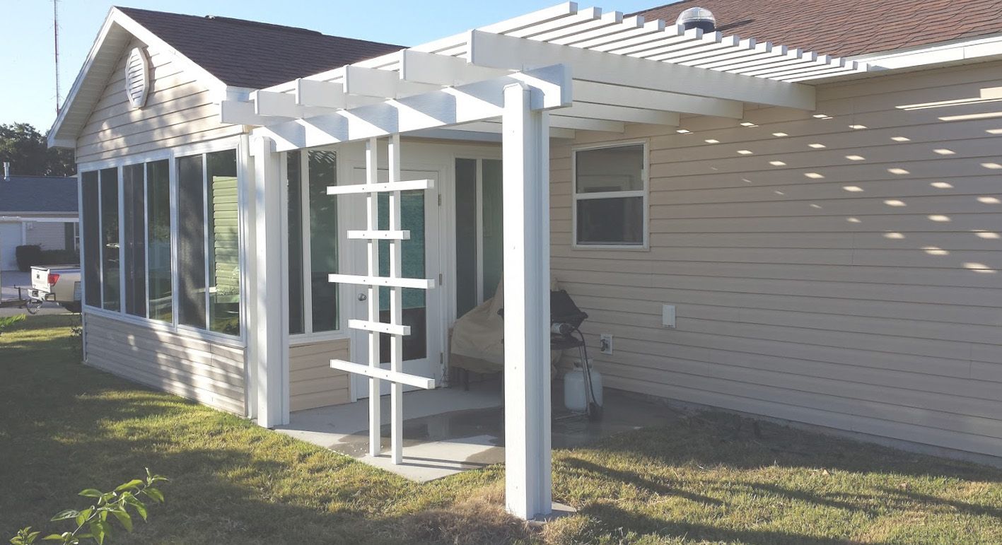 A white pergola is attached to the side of a house