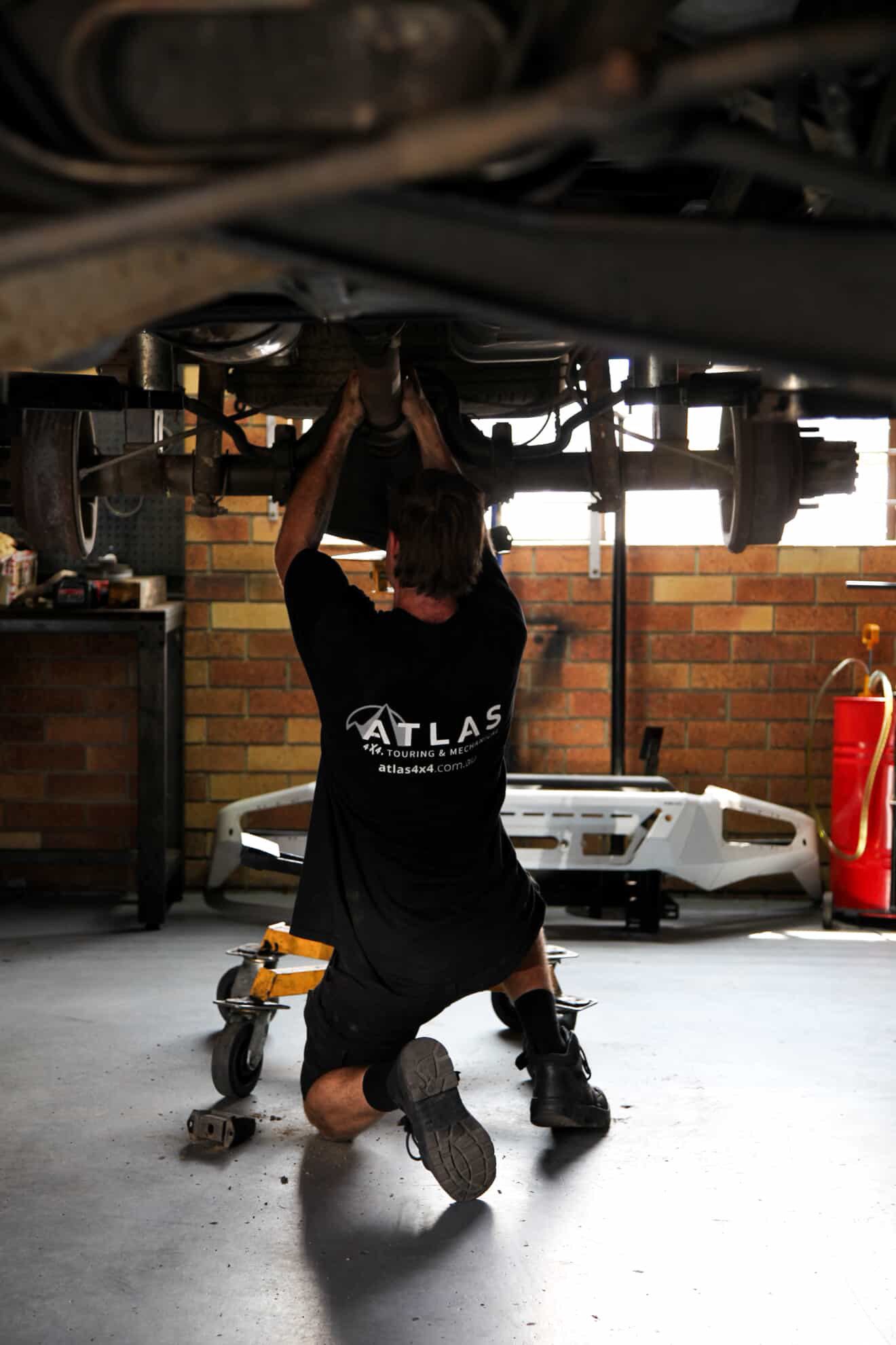 Mechanic working under a car, kneeling — Atlas 4X4 Touring & Mechanical in Tweed Heads, NSW