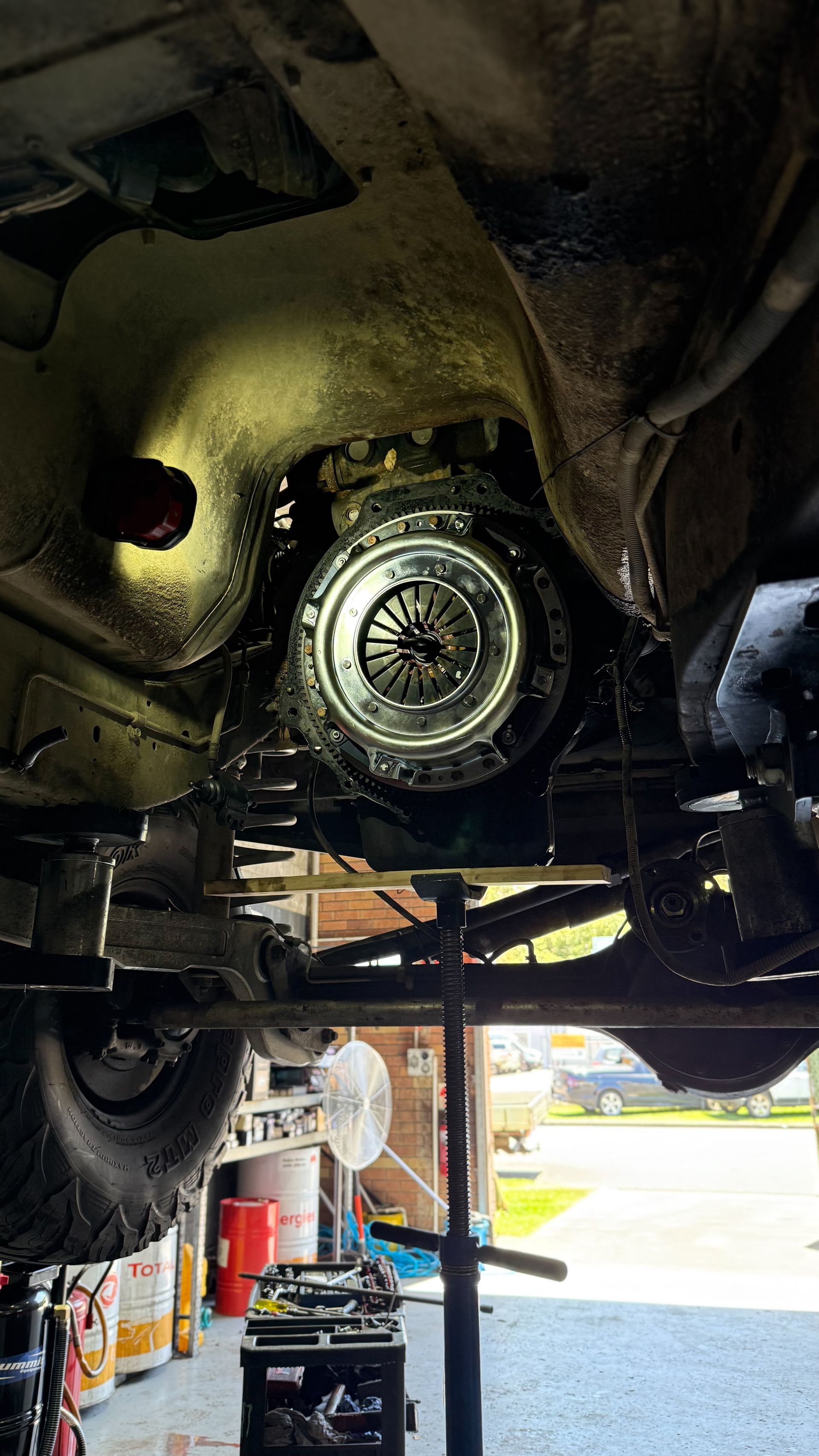 Clutch assembly visible from underneath a vehicle. Bright light illuminates the metal components in a garage setting  — Atlas 4X4 Touring & Mechanical in Tweed Heads, NSW