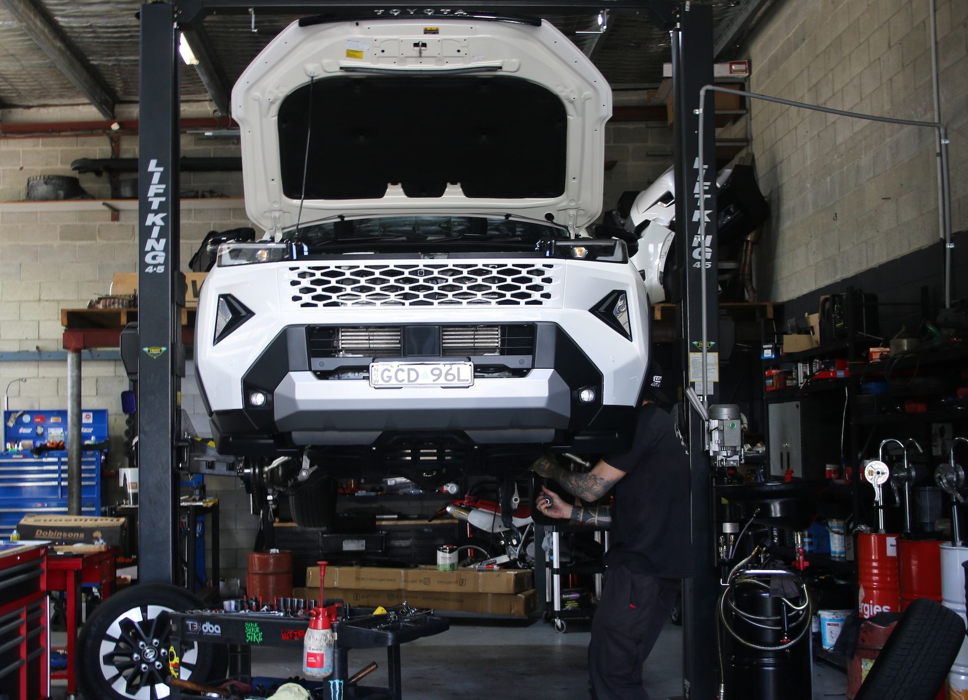White SUV lifted on a car repair lift inside an auto shop with hood open