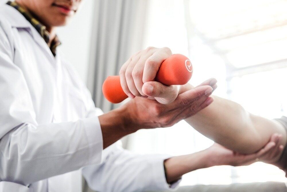 A Doctor Is Helping A Patient With A Dumbbell — Southern Districts Physiotherapy & Sports Injuries Clinic In Albion Park, NSW
