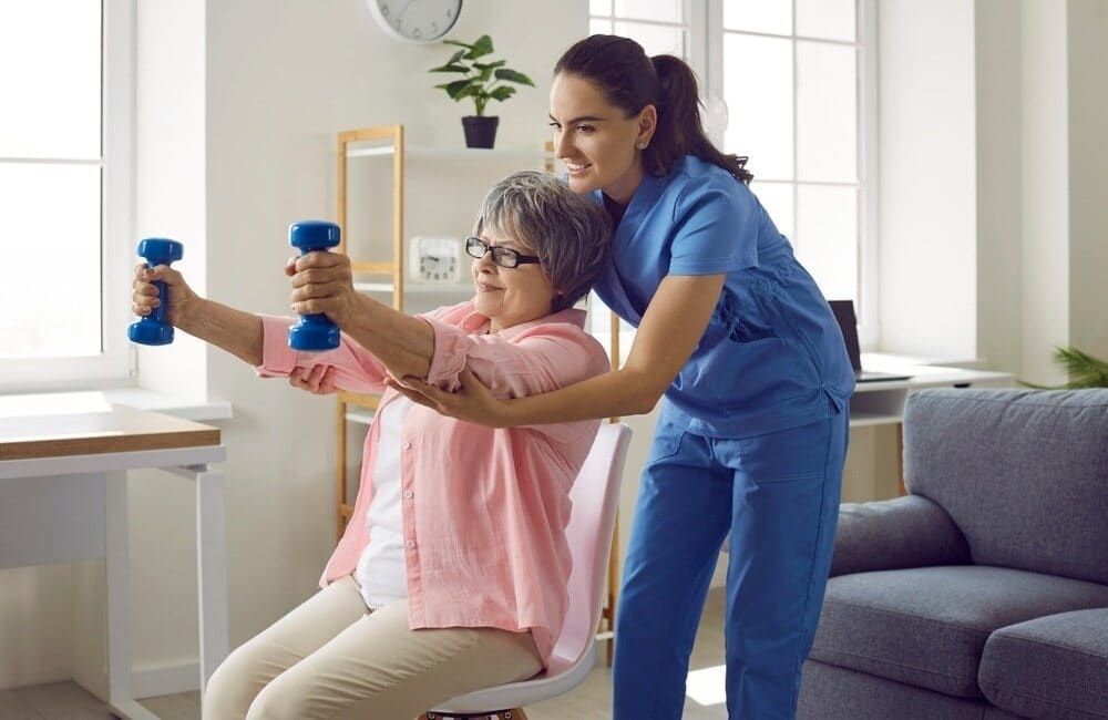 A Nurse Is Helping An Elderly Woman Exercise With Dumbbells — Southern Districts Physiotherapy & Sports Injuries Clinic In Albion Park, NSW