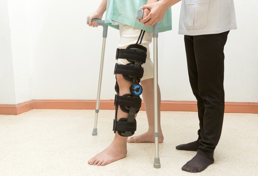 A Man With A Leg Brace And Crutches Is Walking — Southern Districts Physiotherapy & Sports Injuries Clinic In Albion Park, NSW