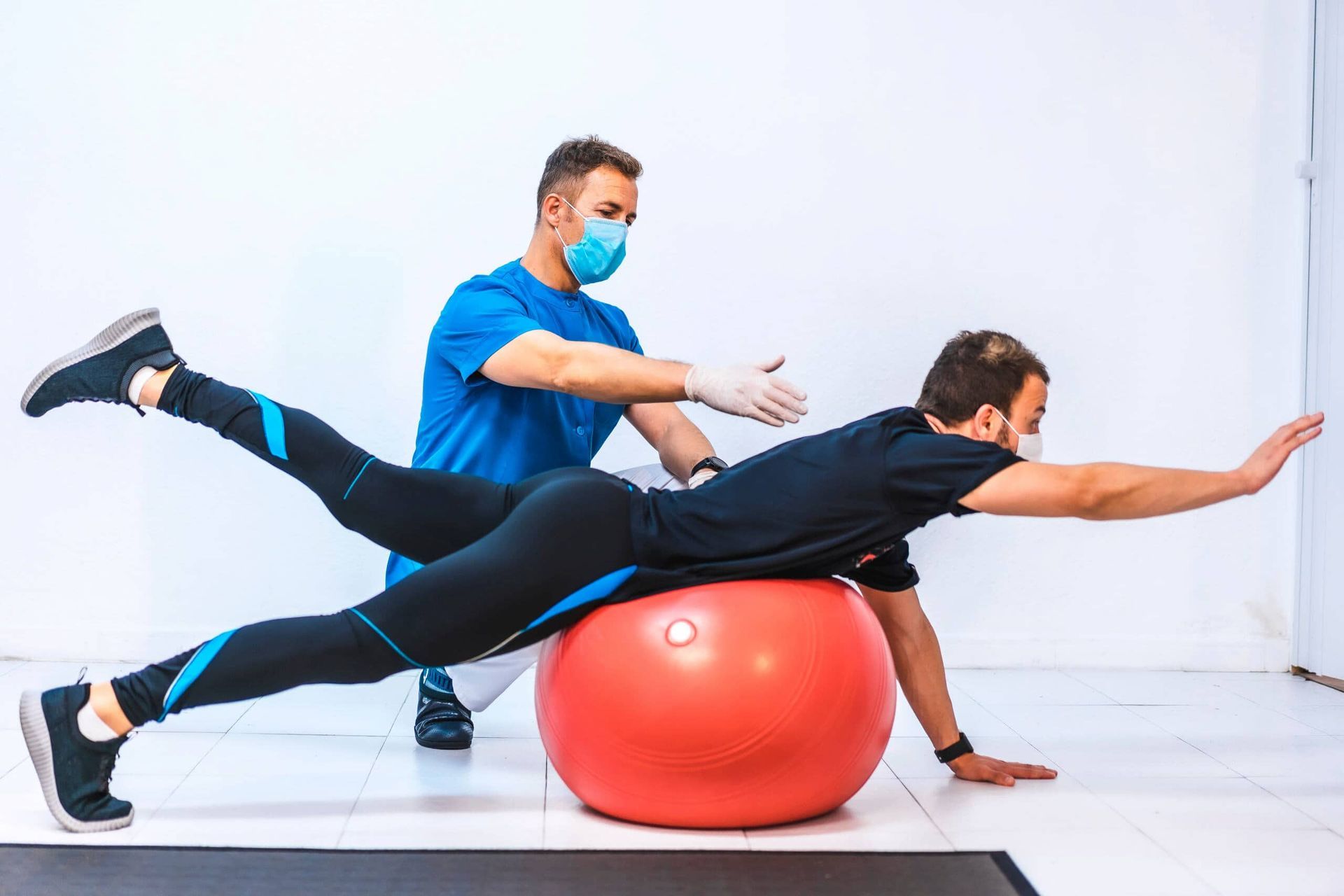 A Man Is Doing Exercises On A Red Exercise Ball While Wearing A Mask — Southern Districts Physiotherapy & Sports Injuries Clinic In Albion Park, NSW