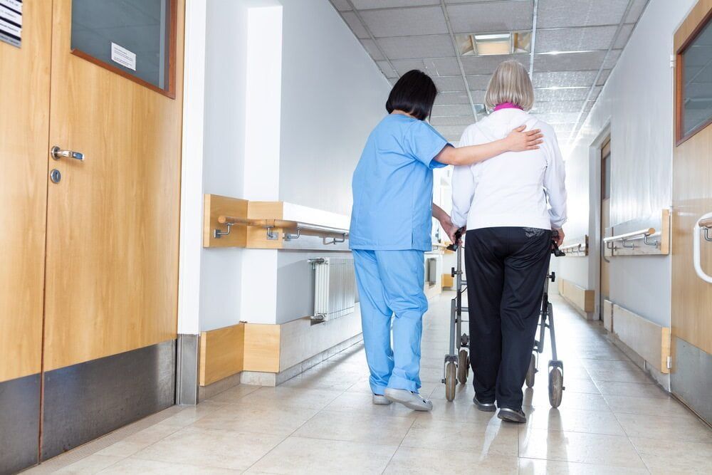 A Nurse Is Helping An Elderly Woman In A Wheelchair Down A Hospital Hallway — Southern Districts Physiotherapy & Sports Injuries Clinic In Tullimbar, NSW