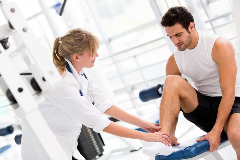 A Man Is Sitting On A Bench While A Female Doctor Examines His Leg — Southern Districts Physiotherapy & Sports Injuries Clinic In Tullimbar, NSW