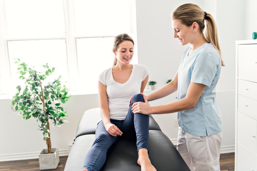 A Woman Is Sitting On A Bed While A Nurse Examines Her Leg — Southern Districts Physiotherapy & Sports Injuries Clinic In Albion Park, NSW