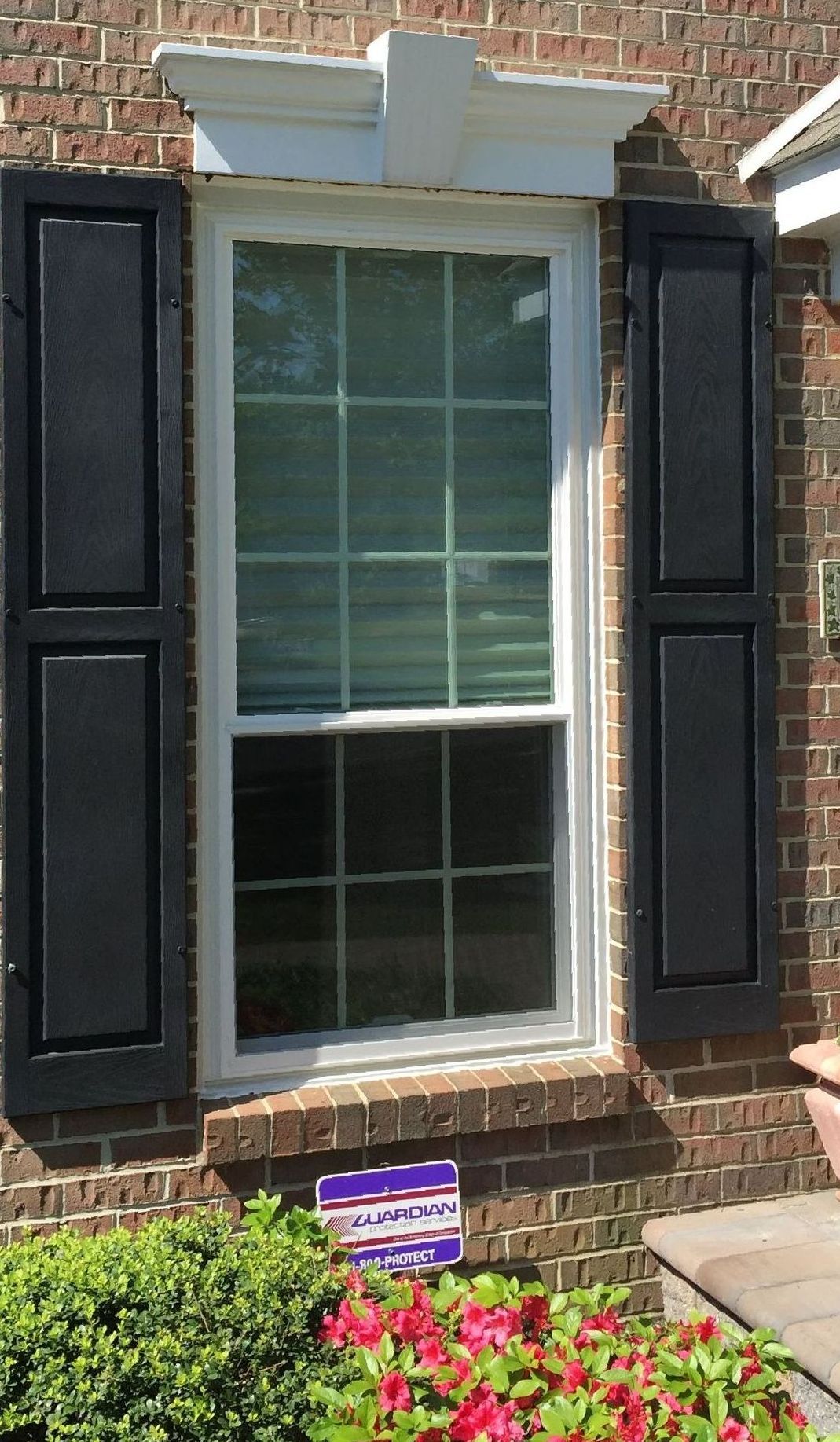 A white window with black shutters on a brick house in Doylestown, PA.