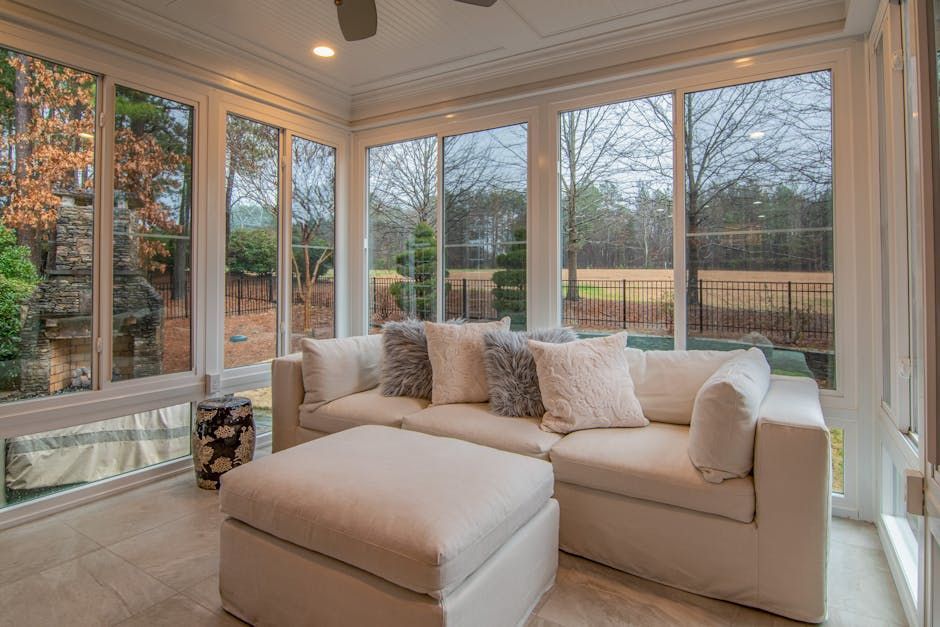 A living room with a couch , ottoman , and lots of windows.