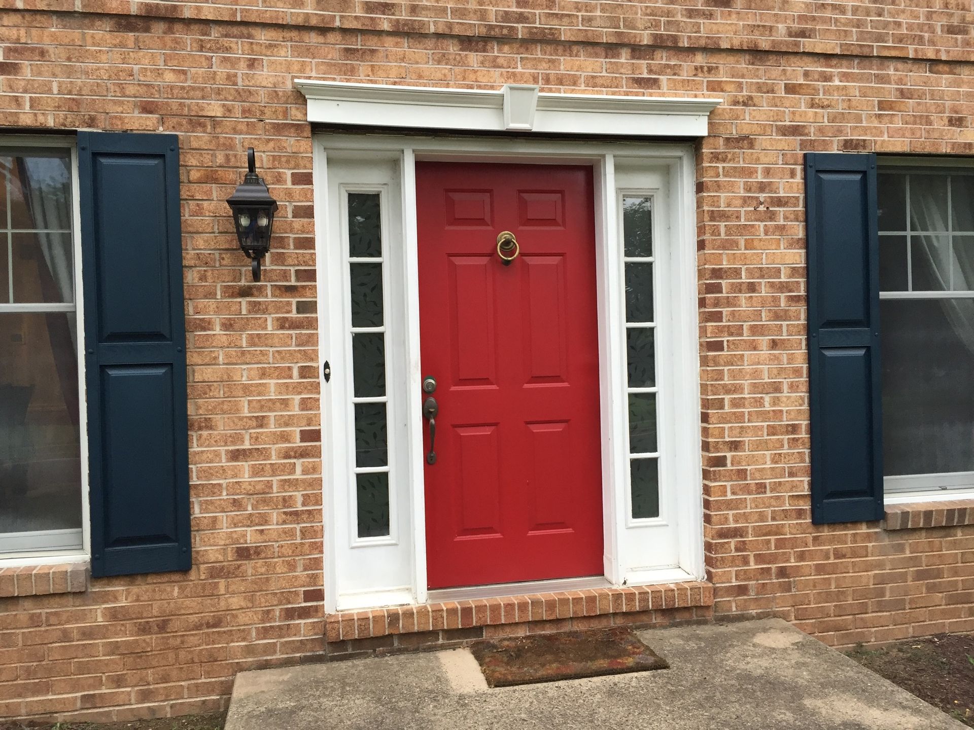 The front door of a brick house with a red door and black shutters.