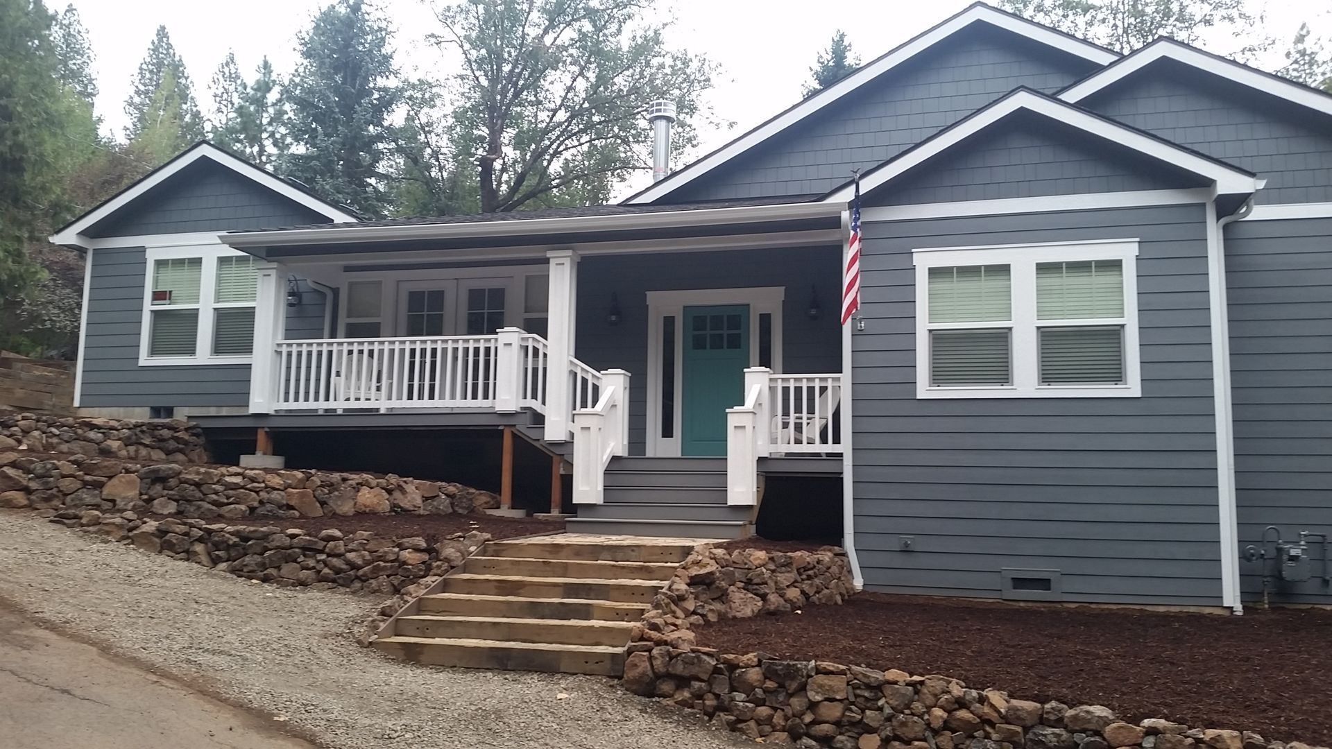 Blue-gray house with a covered porch and a teal door. Stone retaining walls and steps lead up to the entrance.