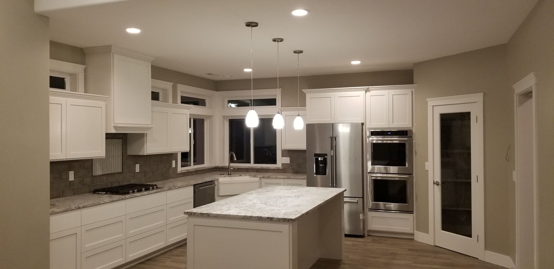 Spacious modern kitchen with white cabinets, stainless steel appliances, and a large island with pendant lights.