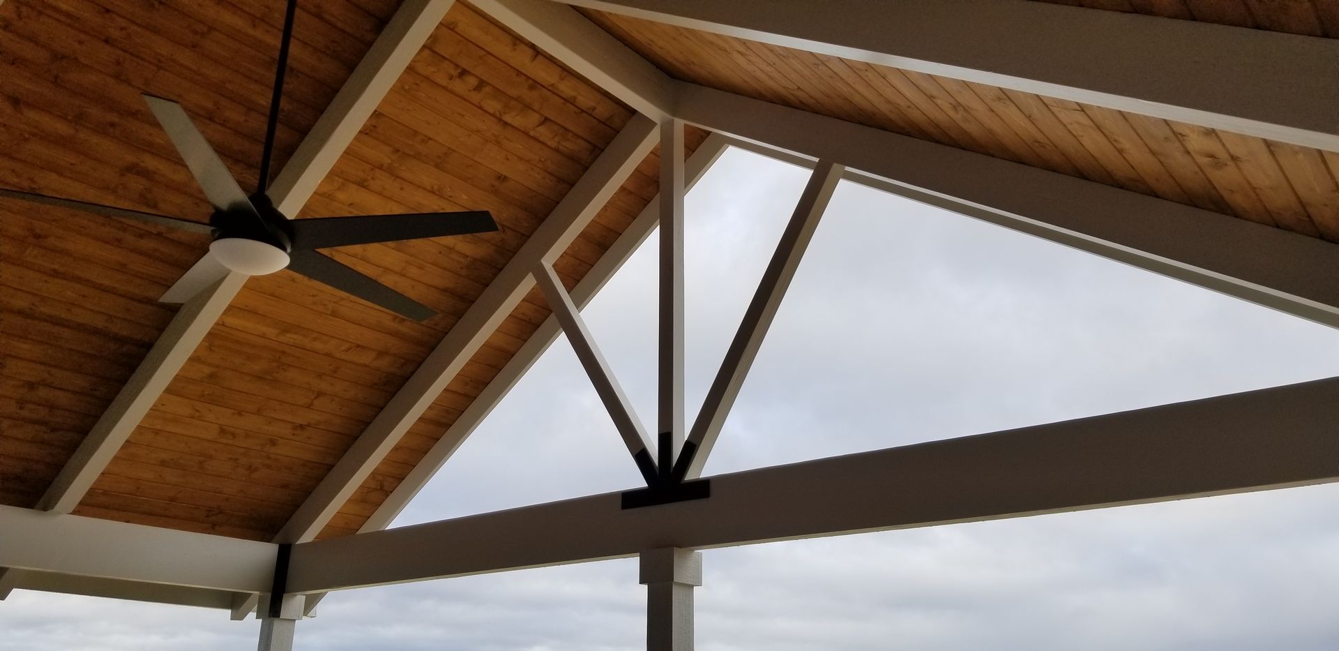 Wooden roof with a ceiling fan and support beams. Sky visible through the frame.