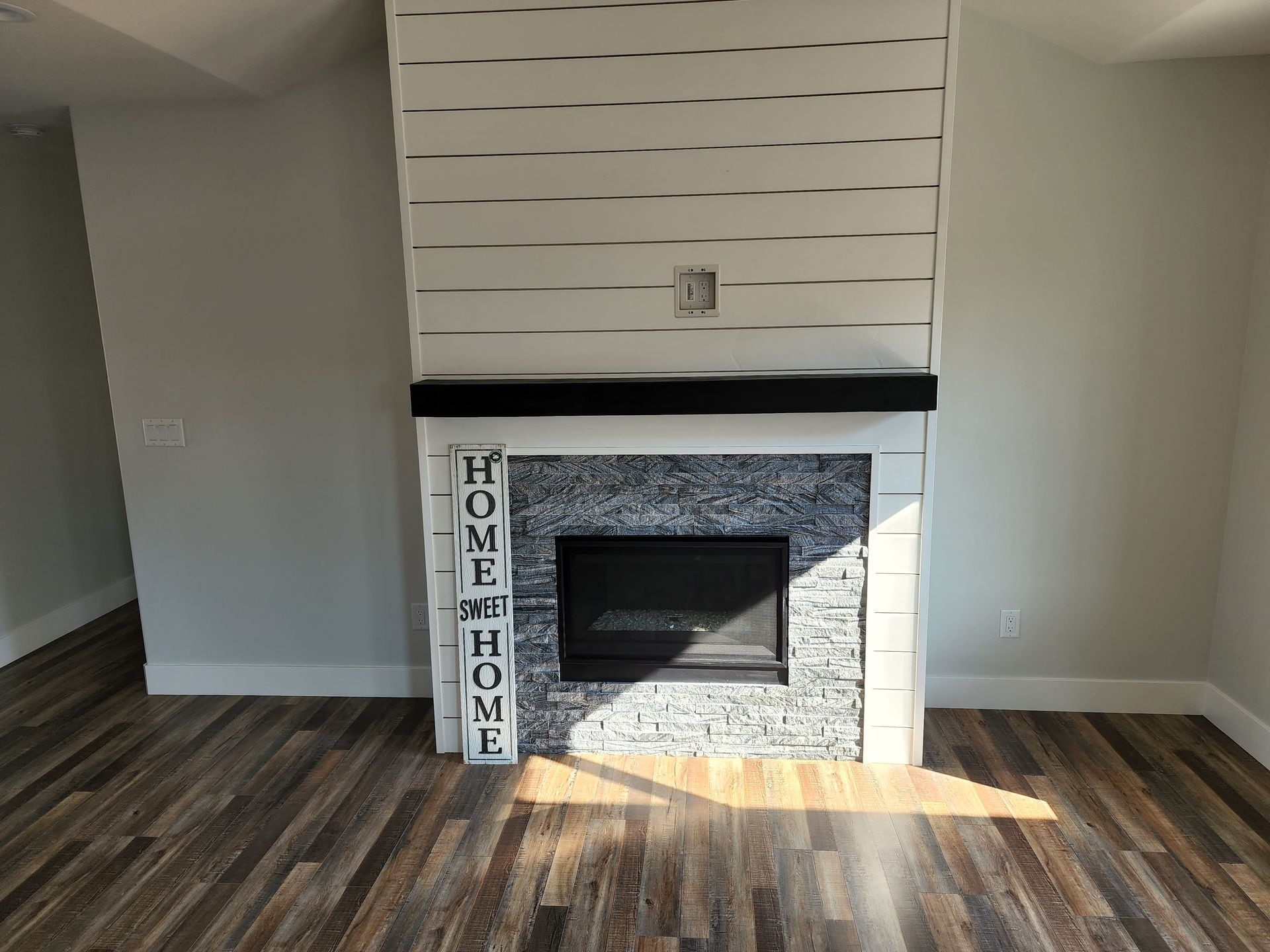 Fireplace with white shiplap surround, black mantel, and stone accent.